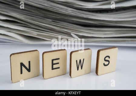 Das Wort news in Brief Fliesen auf einem weiß reflektierend geschrieben mit einem Stapel von alten Zeitungen unscharf im Hintergrund. Aktuelles Konzept Stockfoto