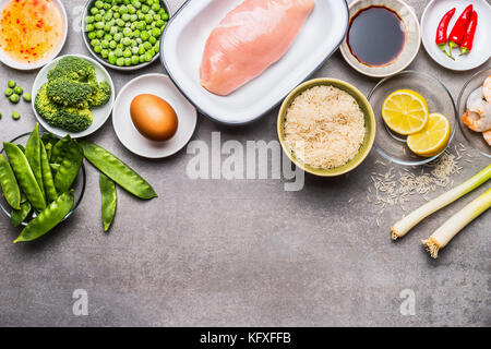 Gebratener Reis Zutaten zum Kochen mit Huhn, Ei, Garnelen und Gemüse auf grauem Stein, Ansicht von oben, Grenze Stockfoto