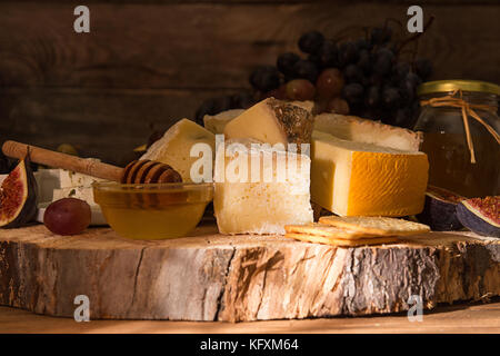 Die Zusammensetzung von Lebensmitteln mit Bausteinen von verschimmelten Käse, eingelegte Rosinen, Honig, Wein, Oliven, Feigen, Birnen, Cracker auf alten Holz- Hintergrund. Ansicht von vorn Stockfoto