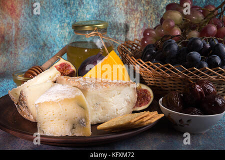 Die Zusammensetzung von Lebensmitteln mit Bausteinen von verschimmelten Käse, eingelegte Pflaumen, Traubenmost, Bündel, Cracker, Feigen auf Blau roten Hintergrund. Stockfoto