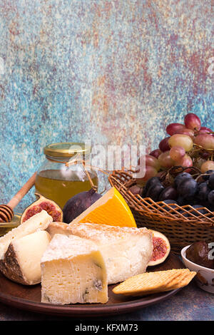 Die Zusammensetzung von Lebensmitteln mit Bausteinen von verschimmelten Käse, eingelegte Pflaumen, Traubenmost, Bündel, Cracker, Feigen auf Blau roten Hintergrund. Platz kopieren Stockfoto