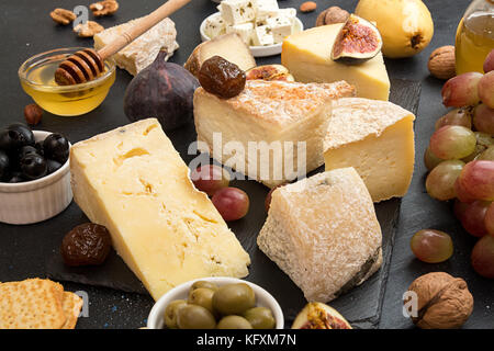 Die Zusammensetzung von Lebensmitteln mit Bausteinen von verschimmelten Käse, eingelegte Rosinen, Honig, Wein, Oliven, Feigen, Cracker, Feigen auf schwarzen Hintergrund. Stockfoto