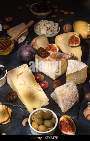 Die Zusammensetzung von Lebensmitteln mit Bausteinen von verschimmelten Käse, eingelegte Rosinen, Honig, Wein, Oliven, Feigen, Cracker, Feigen auf schwarzen Hintergrund. Stockfoto