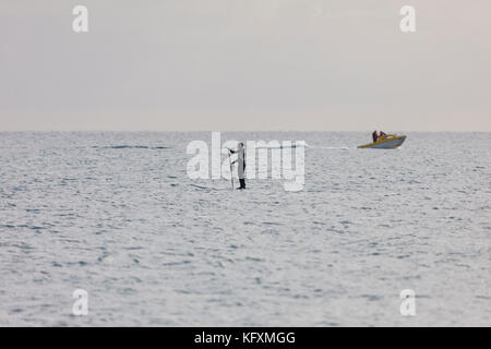 Paddel boarder Paddel Offboarding der Hastings Küste im ruhigen Wasser, Schnellboot im Hintergrund, East Sussex Stockfoto