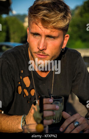 Hübscher blonder junger Mann in Turin cafe Holding Glas sitzen in schwarzen T-Shirt weg schauen. Stockfoto