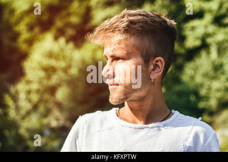 Traurig, besorgt blonde junge Mann gegen Bäume, draussen in der Natur, auf der Suche nach a-Seite Stockfoto