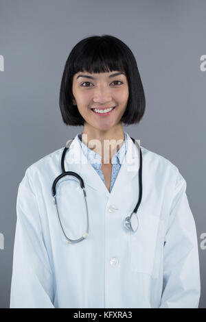Portrait von zuversichtlich Arzt stehend gegen grauer Hintergrund Stockfoto