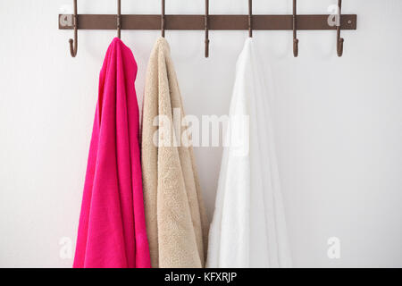 Bunte Handtücher hängen an Haken gegen weiße Wand Stockfoto