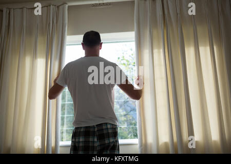 Rückansicht des Menschen öffnen Fenster Vorhang im Schlafzimmer Stockfoto