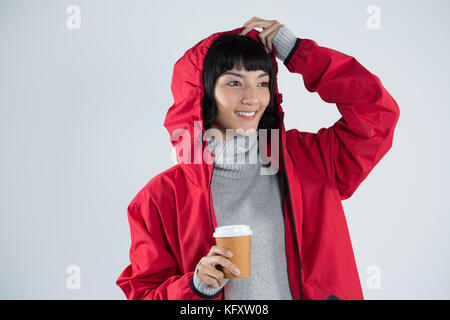 Lächelnde Frau in der roten Jacke mit Kaffee gegen den weißen Hintergrund Stockfoto