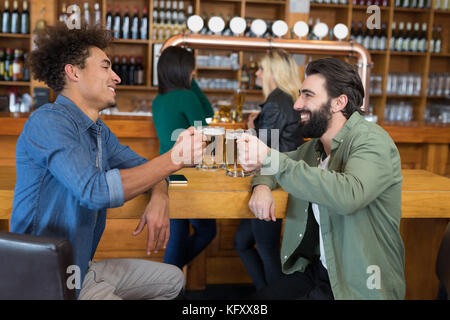 Lächelnd zwei Freunde toasten Glas Bier an der Theke in der Bar Stockfoto