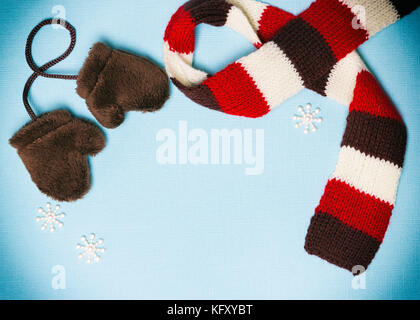 Zusammensetzung der kleine Pelz Fäustlinge, strickschal und kleine Schneeflocken auf Blau strukturierten Hintergrund. Cute winter Rahmen mit leeren Raum für Text Stockfoto