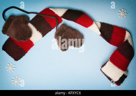 Zusammensetzung der kleine Pelz Fäustlinge, strickschal und kleine Schneeflocken auf Blau strukturierten Hintergrund. Cute winter Rahmen mit Kopie Raum Stockfoto
