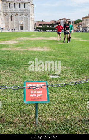 Asiatische Touristen in Pisa, Italien, halten sich nicht an das Schild, um vom Gras fernzubleiben Stockfoto