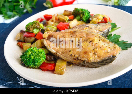Steaks von würzigen Fisch gebraten, serviert mit einem warmen Salat auf einer Keramikplatte auf weißem Holz- Hintergrund. Stockfoto