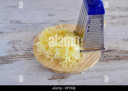 Geriebenen Käse auf einem hölzernen Schneidebrett mit Reibe. Schritt für Schritt kochen Stockfoto