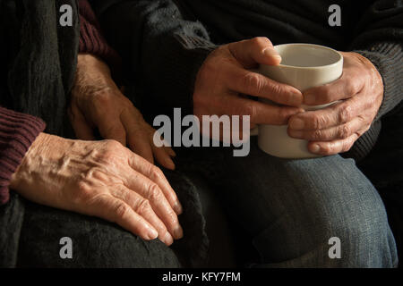 Hände einer alten Frau und ein alter Mann mit einem Becher Stockfoto