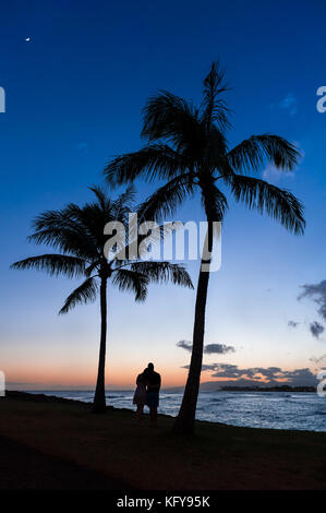 Silhouette von ein paar beobachten einen wunderschönen tropischen hawaiianischen Sonnenuntergang über dem Pazifischen Ozean in Magic Island auf Oahu, HI. Stockfoto