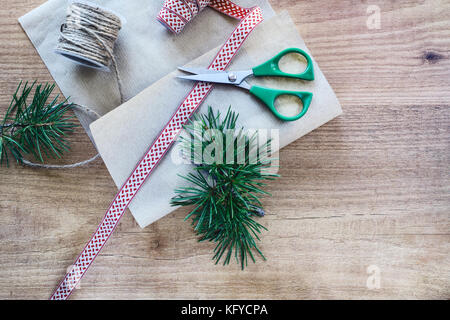 Wickelvorgang der Weihnachtsgeschenke mit rustikalen Papier und Farbband auf abstracts Holz- Hintergrund. Platz für Tex und Kopieren Stockfoto