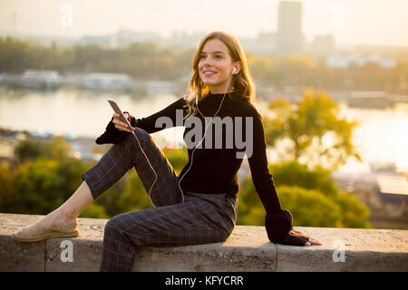 Trendige junge Frau hört Musik von Smartphone outdoor bei Sonnenuntergang Stockfoto