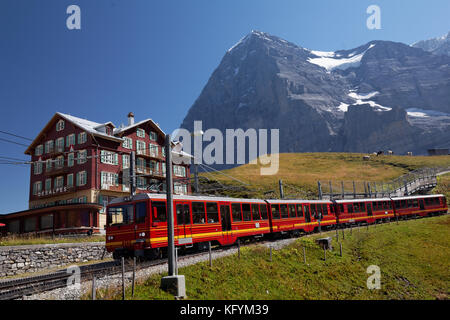 Die roten Eisenbahnwaggons der Jungfrau-Bahn fahren am Hotel des Alps unter der Nordseite des Eigers in der kleinen Scheidegg, Berner Oberland, Schweiz, vorbei Stockfoto