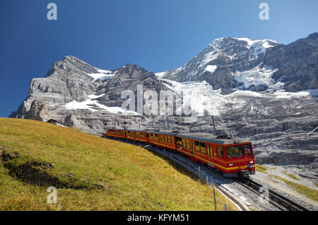 Rote Schienenfahrzeuge auf der Jungfrau-Bahn fahren unterhalb der Nordwand des Eiger-, Mönch- und Jungfrau-Gebirges, Berner Oberland, Schweiz Stockfoto