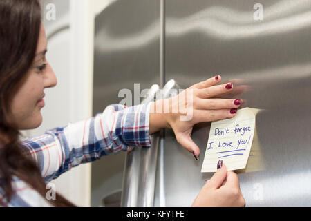 Attraktive 20-25 jährige Weiblich klemmt eine liebe Hinweis auf dem Kühlschrank. Stockfoto