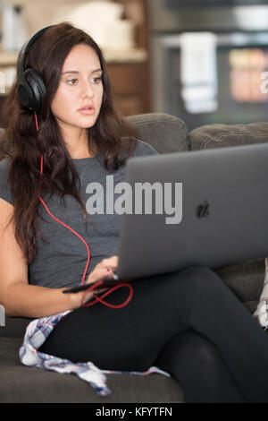 Attraktive 20-25 Jahre alten weißen Frau sitzt auf der Couch und höre Musik. Stockfoto