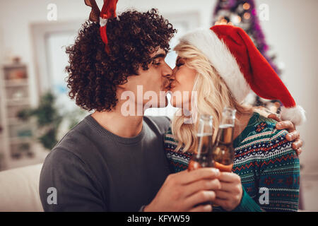 Junge romantische Paar umarmen und küssen in der Weihnachtszeit. Sie Toasten mit Flaschen trinken. Stockfoto