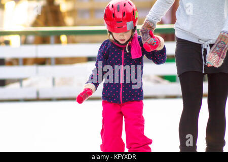 Eine junge Frau mit ihrer Tochter Schlittschuhlaufen auf der Eisbahn. Stockfoto