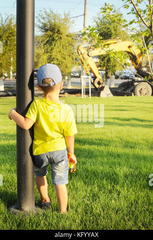 Der junge beobachtet die Arbeit der Bagger, hält ein Spielzeug Bagger in der Hand, das Konzept Stockfoto