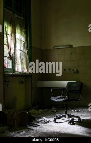 Ein furchtsames geschossen von einem Stuhl in der Dunkelheit, in einem Raum eines verlassenen psychiatrischen Krankenhaus, mit einem unheimlichen Umgebung. Stockfoto