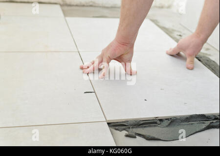 Festlegung von Keramikfliesen. Troweling Mörtel auf Betonboden in der Vorbereitung für die Verlegung von weißen Bodenfliesen. Stockfoto