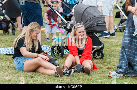 Zwei junge Frauen, die auf dem Boden sitzend an der Coventry Godiva Music Festival, Coventry, West Midlands, UK. Stockfoto