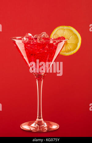 Glas mit red Cocktail, Zitronenscheibe und Eiswürfel auf rotem Hintergrund. Stockfoto