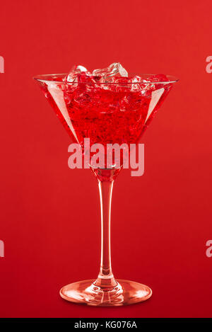 Glas mit red Cocktail und Eiswürfel auf rotem Hintergrund. Stockfoto