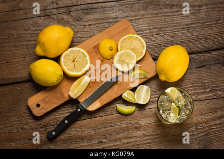 Zitronen, Messer und Zitronenscheiben auf Schneidebrett, mit Wasser, Glas auf Holz- Tabelle. Stockfoto