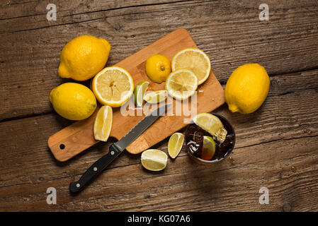 Zitronen, Messer und Zitronenscheiben auf Schneidebrett, mit cocacola Glas auf Holz- Tabelle. Stockfoto