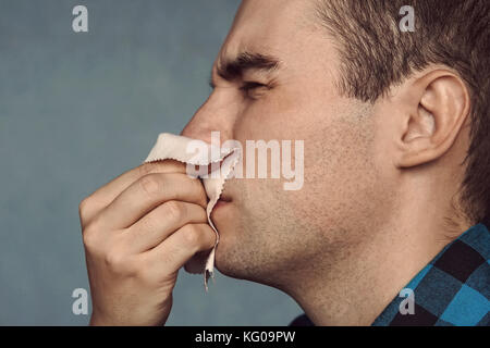 Der Mann hat eine laufende Nase. Ein junger Kerl niest in einem rosa Schal auf einem blauen Hintergrund. erkältungen im Herbst. Rotz aus der Nase. Stockfoto