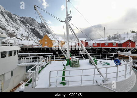 Schnee bedeckt Hafen - Fischerdorf nusfjord - alte hölzerne Fischerboote - bottelvika Bucht - nesheia+sultinden mts. - Rot + orange Fischerhütten oder Rorbuer für Stockfoto