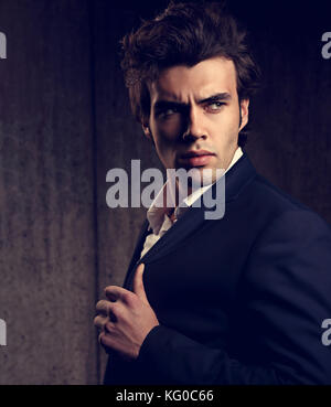 Zuversichtlich stattlicher Mann mit dem belasteten Look in Blau mode Anzug und weissen style Hemd auf dunklen Schatten Hintergrund posiert. Closeup Ton portrait Stockfoto