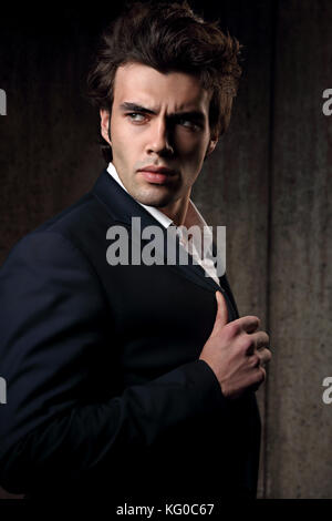 Zuversichtlich stattlicher Mann mit dem belasteten Look in Blau mode Anzug und weissen style Hemd auf dunklen Schatten Hintergrund posiert. Closeup Portrait Stockfoto