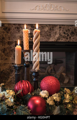 Wohnzimmer für Weihnachten mit angezündeten Kerzen dekoriert, Holly, und rote Kugel Verzierungen auf dem Tisch vor dem Kamin Stockfoto