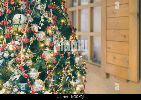 Dekorierte und beleuchtete Weihnachtsbaum gegen Holzhaus. selektive Fokus, getönten Bild Stockfoto