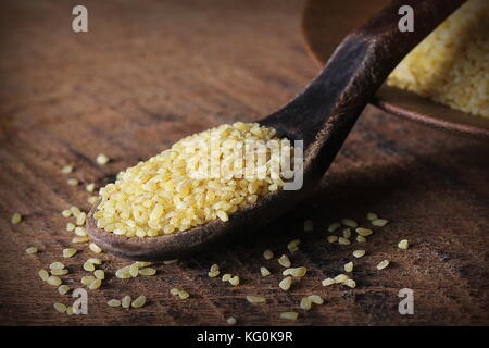 Trockene Bulgur weizen in hölzernen Löffel auf rustikalen Hintergrund. verschüttet Bulgur Stockfoto