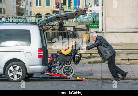 Mann drücken behindertes Kind in einen Rollstuhl, eine Rampe in ein Auto. Stockfoto