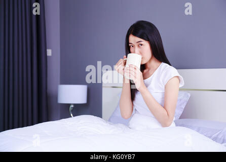 Frau im Bett mit einer Tasse Kaffee im Schlafzimmer Stockfoto