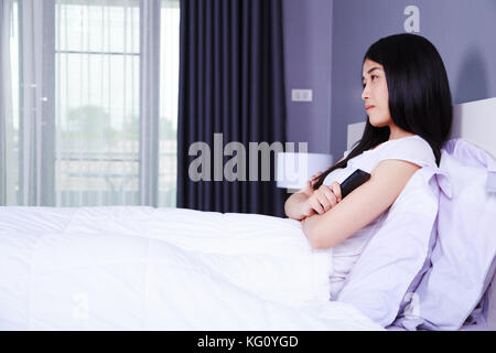 Frau Fernsehen mit Fernbedienung auf dem Bett im Schlafzimmer Stockfoto