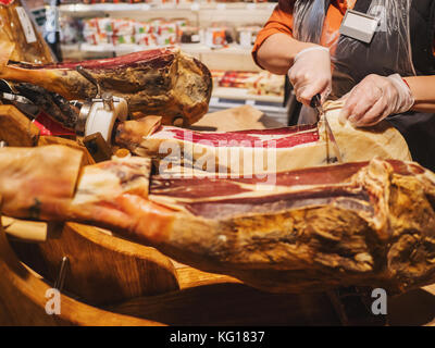 Hände einer Frau in der Handschuhe auf dem Markt oder schneiden Sie ein Stück vom traditionell spanischen Jamón de Bellota. Fleisch hautnah. Stockfoto