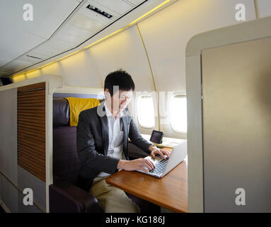 Asiatischer Mann arbeiten mit Laptop auf first class Flugzeug Stockfoto